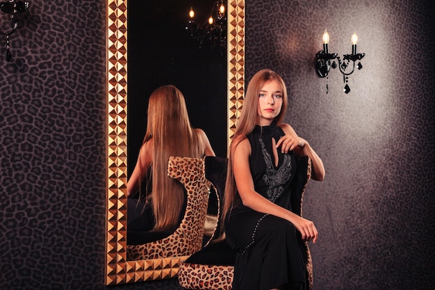 Portrait of pretty cute teenager girl in an elegant dress at mirror