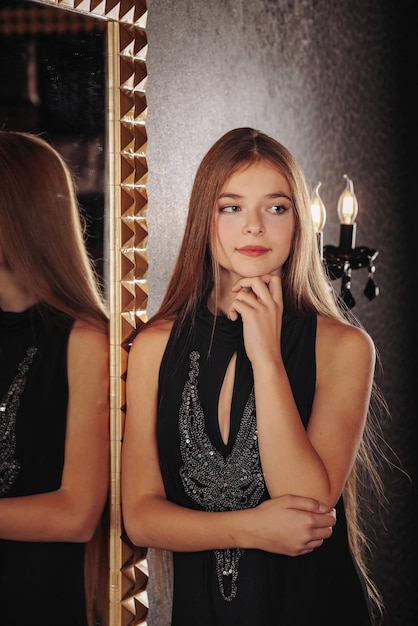 Ritratto di ragazza adolescente piuttosto carina in un vestito elegante allo specchio
