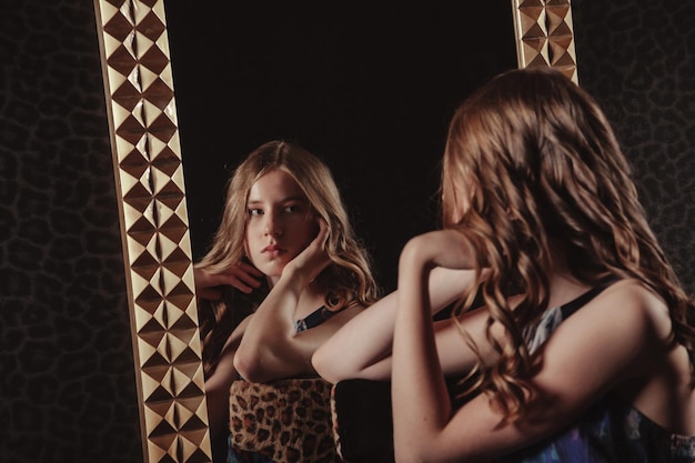 Portrait of pretty cute teenager girl in an elegant dress at mirror