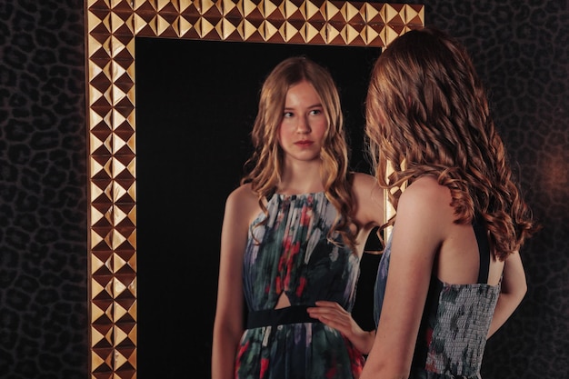 Portrait of pretty cute teenager girl in an elegant dress at mirror