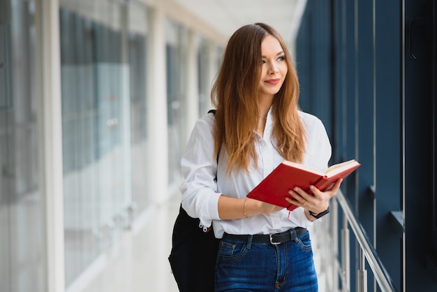 Portrait of a pretty female student with books and a backpack in the university hallway