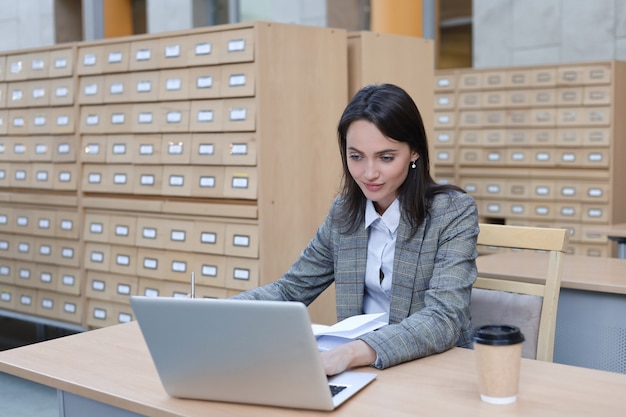 Portrait of a pretty female student with laptop in library.