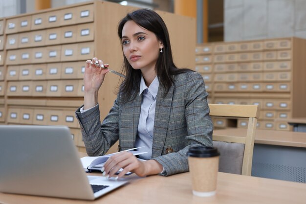 Portrait of a pretty female student with laptop in library.