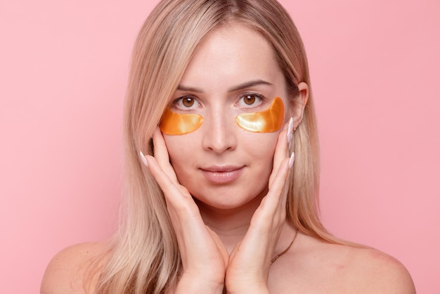 Photo portrait of pretty girl applying golden collagen patches under her eyes in unusual way woman facial treatment cosmetology beauty and skincare around eyes preventing wrinkles