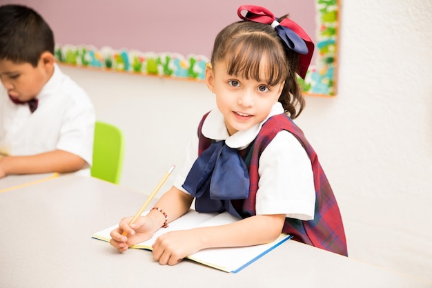 Portrait of a pretty girl attending preschool and wearing a uniform in a classroom