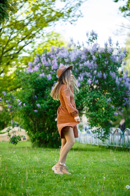 Portrait of a pretty girl in a brown hat with a lilac in the garden