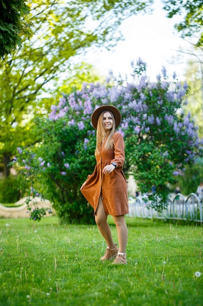 Portrait of a pretty girl in a brown hat with a lilac in the garden