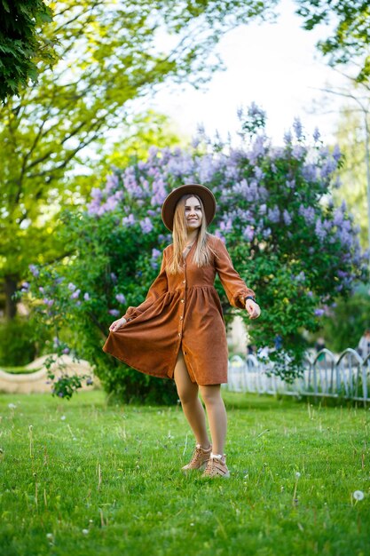 Portrait of a pretty girl in a brown hat with a lilac in the garden