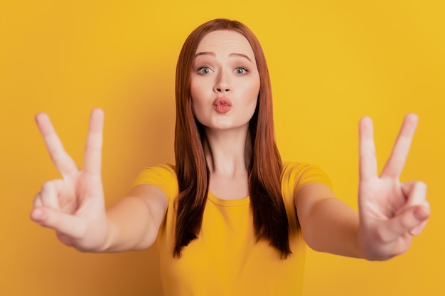 Portrait of pretty girl gesturing v-signs send air kiss isolated on yellow background