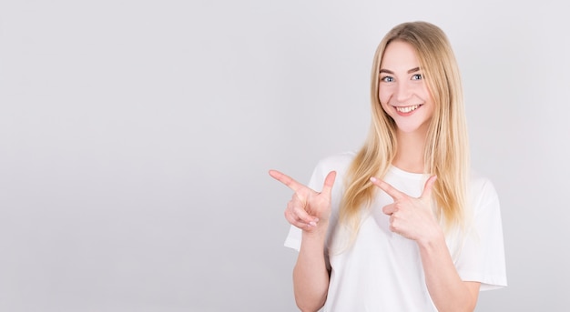 Portrait of a pretty girl pointing finger away on a gray