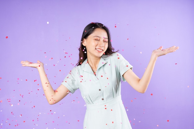 Portrait of a pretty girl standing underneath buying confetti to celebrate, isolated on purple background