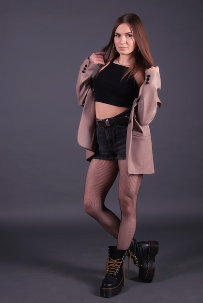 Portrait of a pretty girl wearing black jeans shorts and boots with brown leather jacket. full length