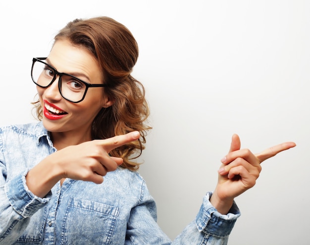 Portrait of a pretty girl wearing glasses pointing finger away isolated on a white background