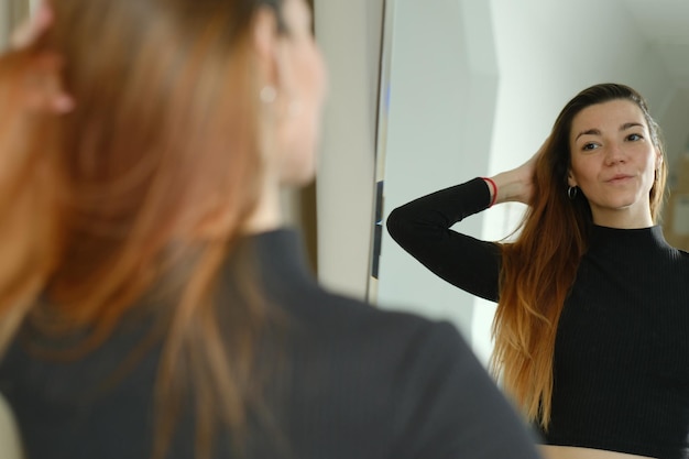 Portrait of a pretty girl with freckles and long red hair at the mirror in the studio