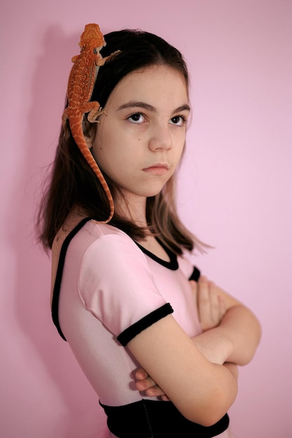 Portrait of pretty girl with Red bearded Agama iguana on pink background Little child playing