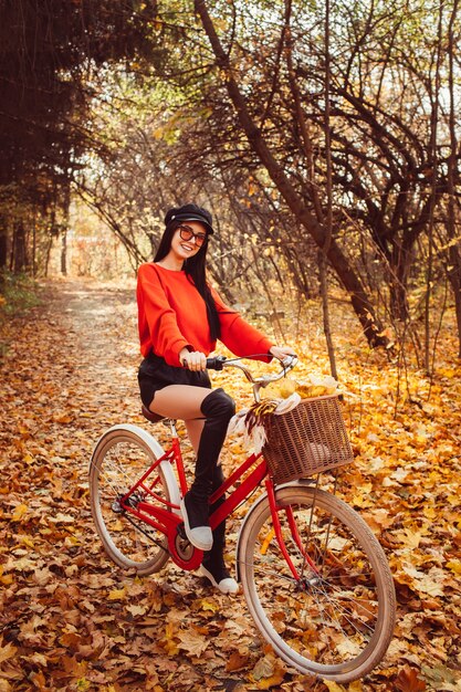 Ritratto di una bella ragazza con una bici rossa nella foresta di autunno