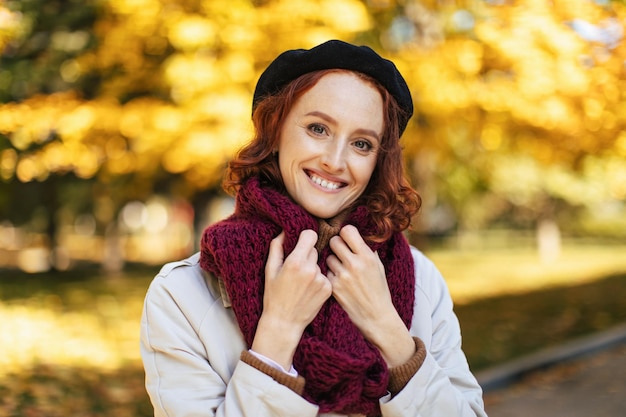 Portrait of pretty happy european millennial redhead lady in raincoat and scarf enjoy warm weather in park