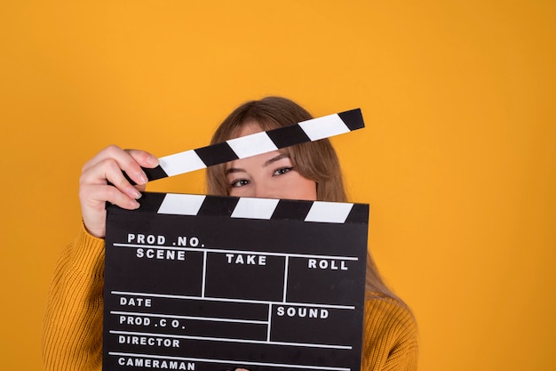 Ritratto di donna bella e felice, sorridente, con ciak, su sfondo giallo-arancione