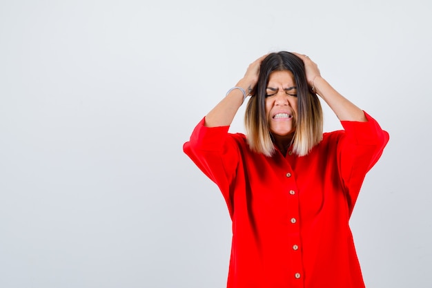 Portrait of pretty lady holding hands on head in red blouse and looking irritated front view