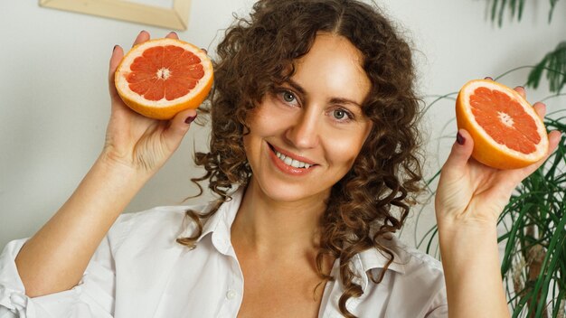 Портрет женщины довольно средних лет с вьющимися волосами с грейпфрутом дома - светлая комната. Понятие счастья, красоты и здоровья