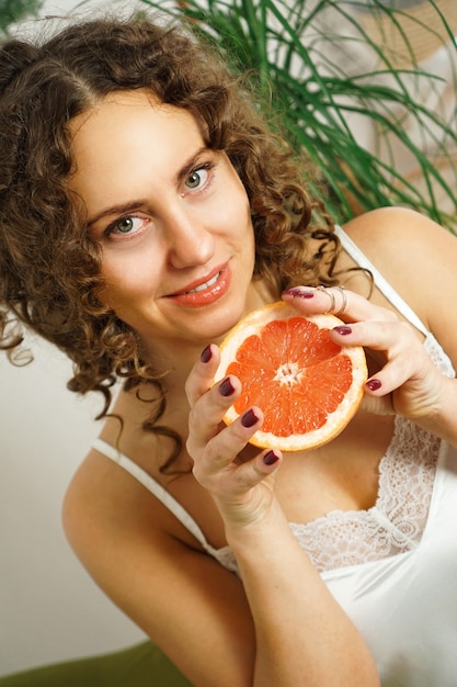 Foto ritratto di una bella donna di mezza età con i capelli ricci con pompelmo a casa - stanza luminosa. felicità, bellezza e salute - foto verticale