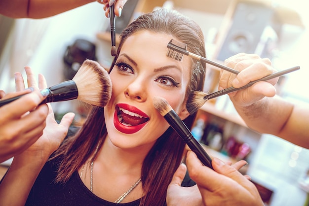 Portrait of a pretty pin-up girl getting make-up applied by a makeup with many  hands. Close-up.