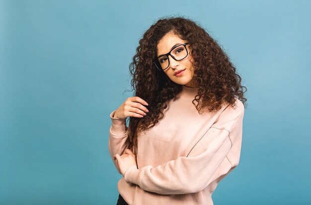 Portrait of a pretty smiling curly young woman in casual posing isolated on a blue background.