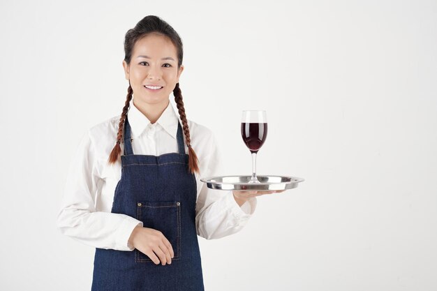 Portrait of pretty smiling female waitress holding glass of wine on metal tray