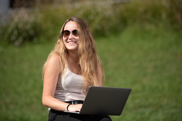 Портрет довольно улыбающейся девочки-подростка, работающей на своем ноутбуке с зеленым фоном