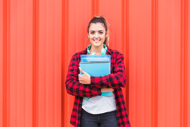 Foto ritratto dello studente grazioso in libri casuali astuti della tenuta a disposizione che stanno contro la parete che guarda alla macchina fotografica