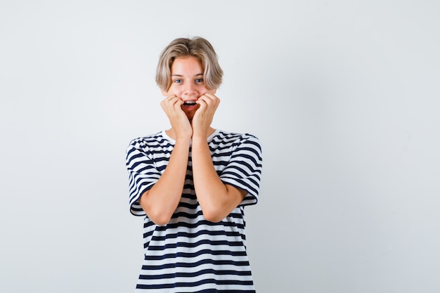 Portrait of pretty teen boy leaning cheeks on hands in striped t-shirt and looking cheerful front view