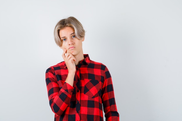 Portrait of pretty teen boy with hand on chin in checked shirt and looking pensive front view