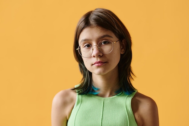 Portrait of pretty teenage girl in eyeglasses looking at camera against orange background