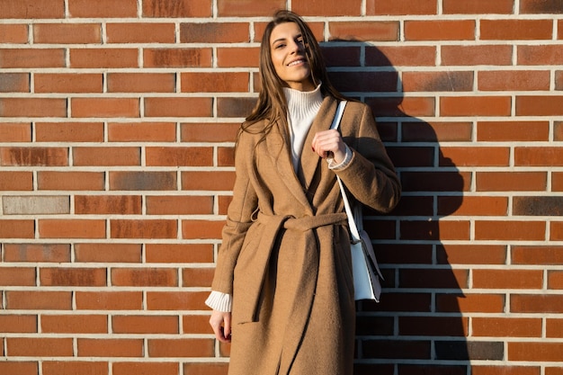 Portrait of pretty woman in brown coat on the background of brick wall