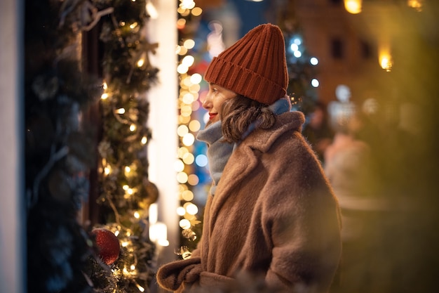 クリスマスマーケットでショーケースを見て、休日の間にダウンタウンを歩いて、休日の贈り物を探しているきれいな女性の肖像画。高品質の写真