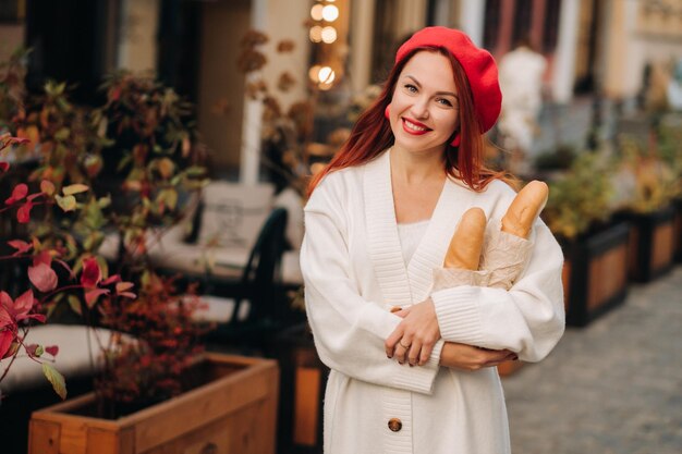 Portrait of a pretty woman in a red beret and a white cardigan\
with baguettes in her hands strolling through the autumn city