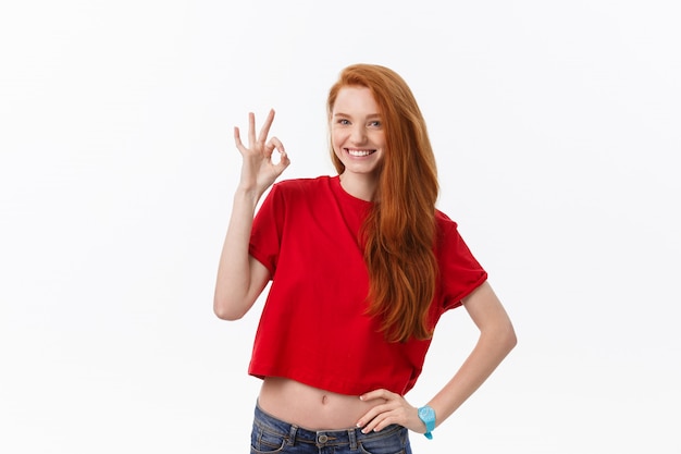 Portrait of a pretty woman in red santa claus dress showing okay sign and winking over white