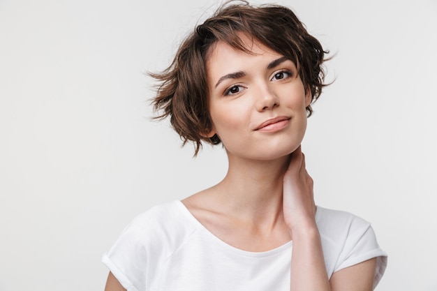 Portrait of pretty woman with short brown hair in basic t-shirt  while standing isolated over white wall