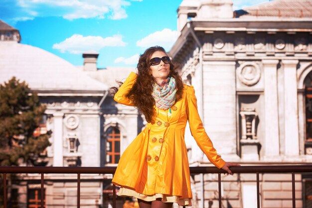 Portrait of a pretty woman in yellow overcoat and sunglasses walking around old city in sunny spring day