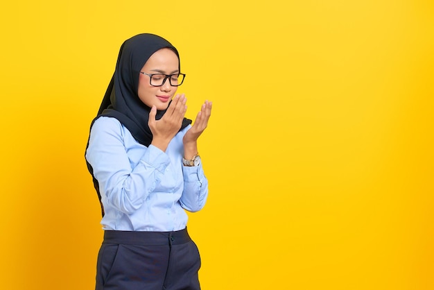 Portrait of pretty young asian woman praying with closed eyes, holding palms face up isolated on yellow background