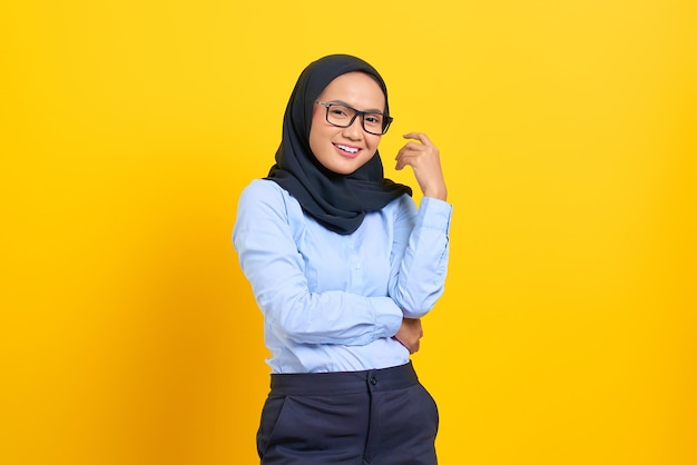 Portrait of pretty young Asian woman smiling happy and looking confident isolated on yellow background