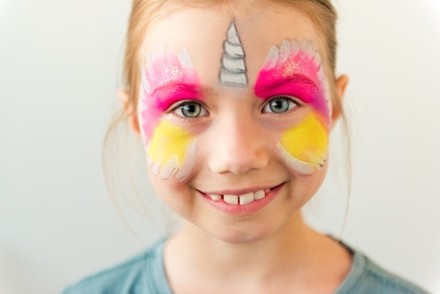 Portrait of pretty young blond girl with face-painting like unicorn