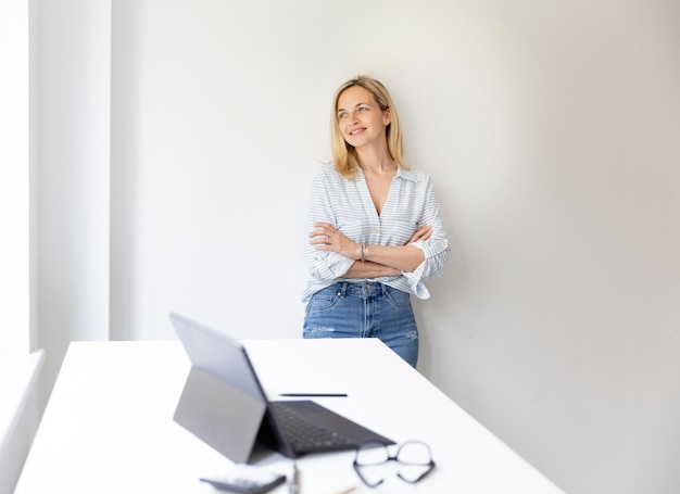 Ritratto di una bella giovane donna d'affari bionda in piedi accanto alla sua scrivania regolabile in altezza ergonomica nel suo ufficio a casa