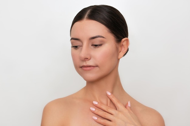 Portrait of a pretty young Caucasian woman gently touching her body isolated on a light background.