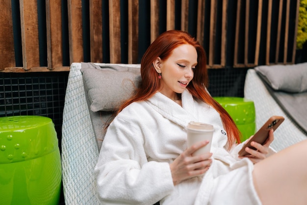 Portrait of pretty young couple in love wearing bathrobe holding glass with freshly squeezed vitamin juice in hands standing hugging looking at camera enjoying relaxation at spa salon