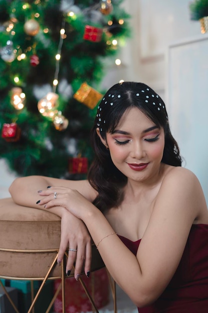 Portrait of pretty young girl cozy sit down on the floor smiling wear red gown in decorated Christmas living room indoors