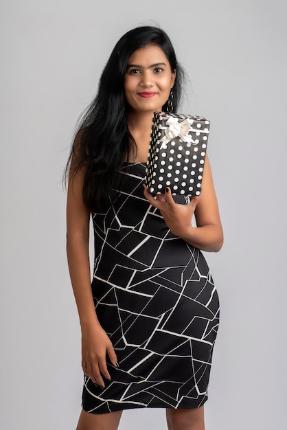 Portrait of a pretty young girl posing with gift box on grey