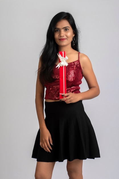 Portrait of a pretty young girl posing with gift box on grey.