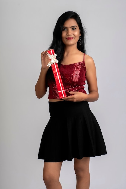 Portrait of a pretty young girl posing with gift box on grey.