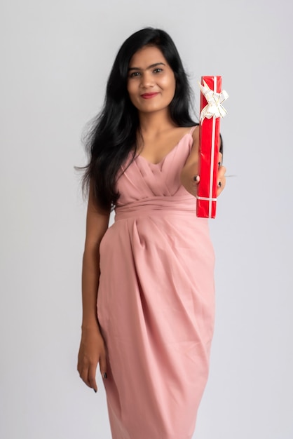 Portrait of a pretty young girl posing with gift box on grey.